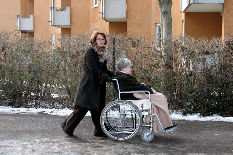 Pflegefachkraft fährt ältere Frau im Rollstuhl spazieren